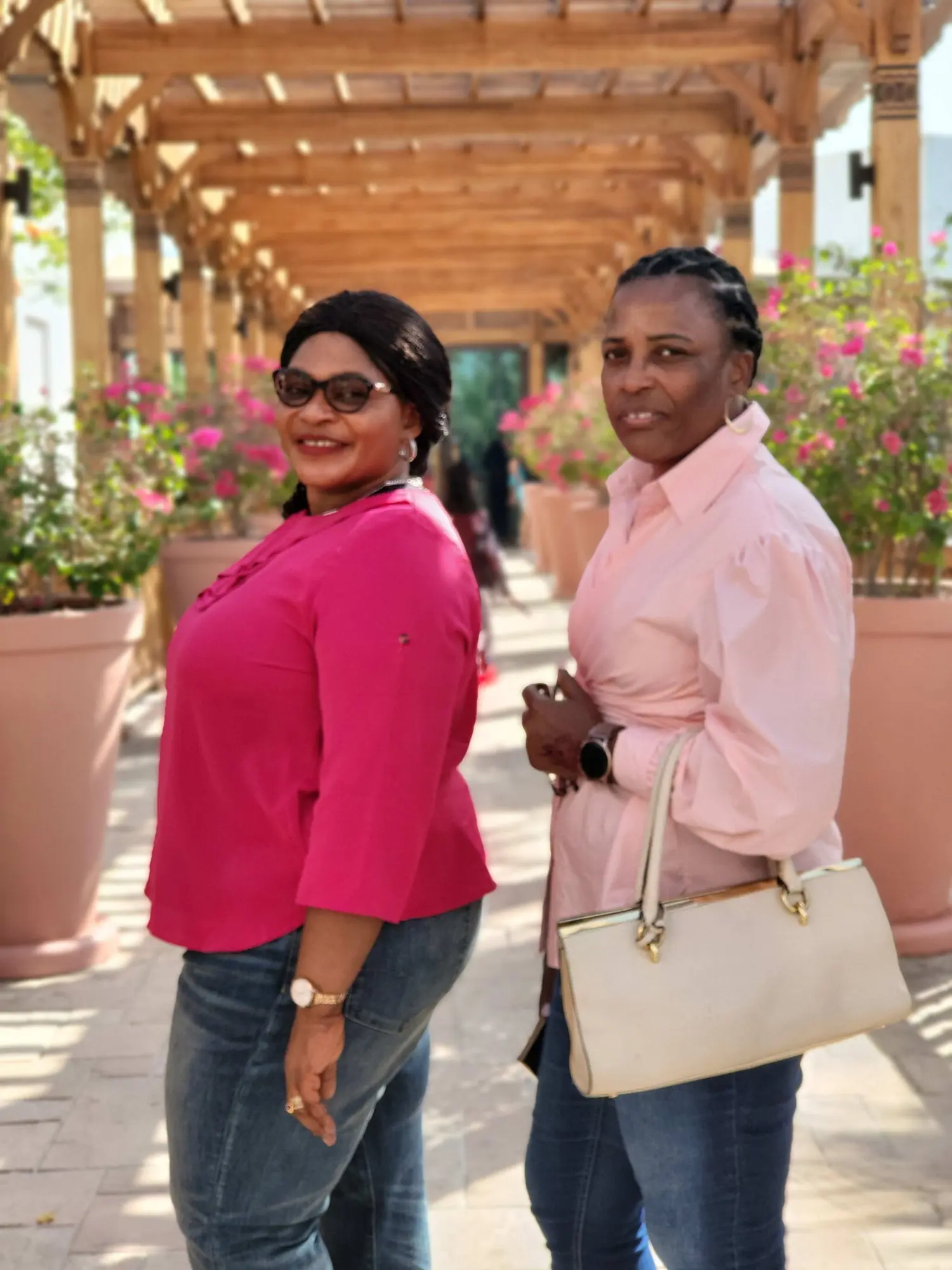 Two women walking a shaded pergola walkway lined with bougainvillea during a Dubai site review