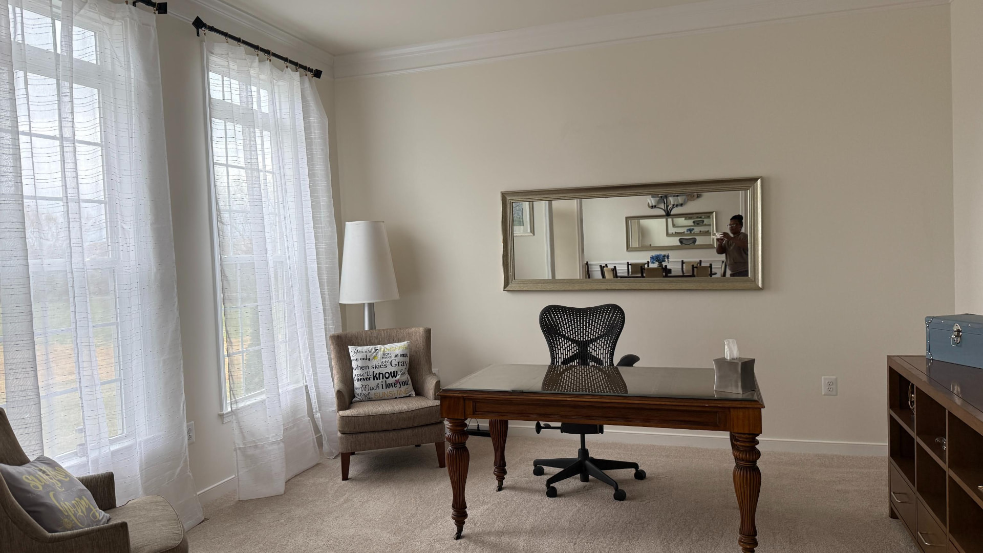 Home office with a wood desk, reading chair and sheer-curtained windows