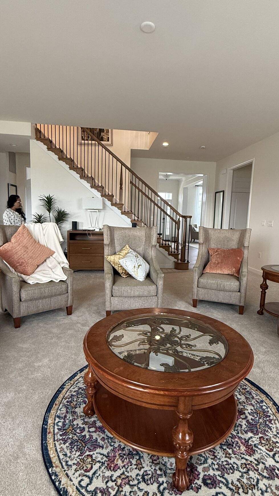 Living room seating group with wingback chairs, round coffee table and staircase beyond